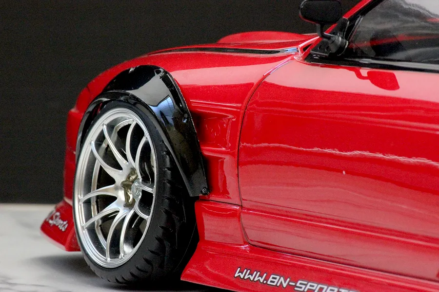 Close-up view of a glossy red RC car body featuring a mounted black over fender set above a silver multi-spoke wheel.