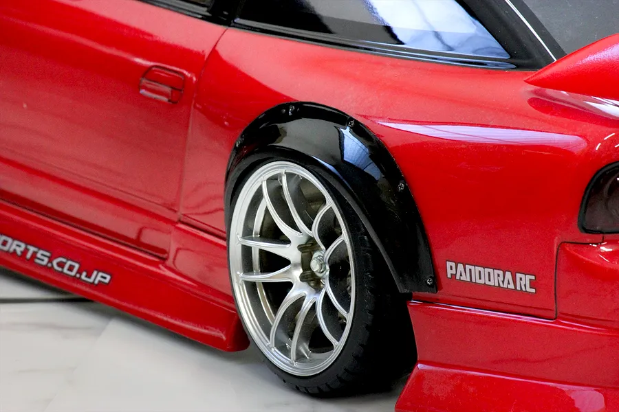 Close-up view of a black over fender set installed on a red RC car body shell with a silver wheel.
