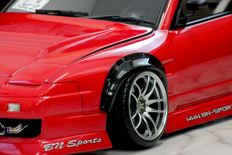 Close-up of a red RC car body shell installed with a black over fender set and chrome multi-spoke wheel.