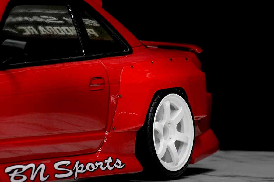 Close-up of a red RC car body showing the rear fender flare installed over the rear wheel, featuring visible mounting screw details.