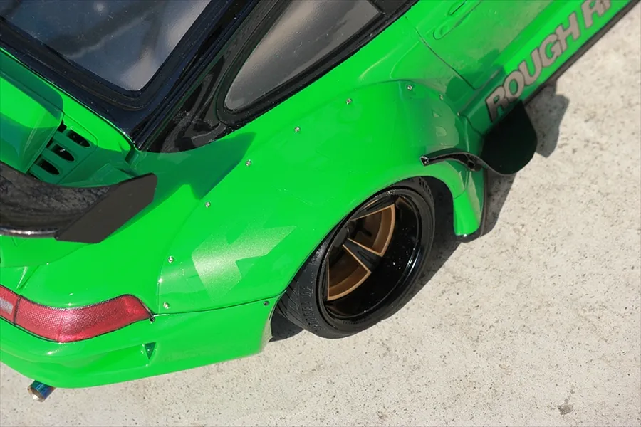 Close-up of a bright green RC car body featuring a wide fender set, rear wheel, and spoiler against a concrete background.