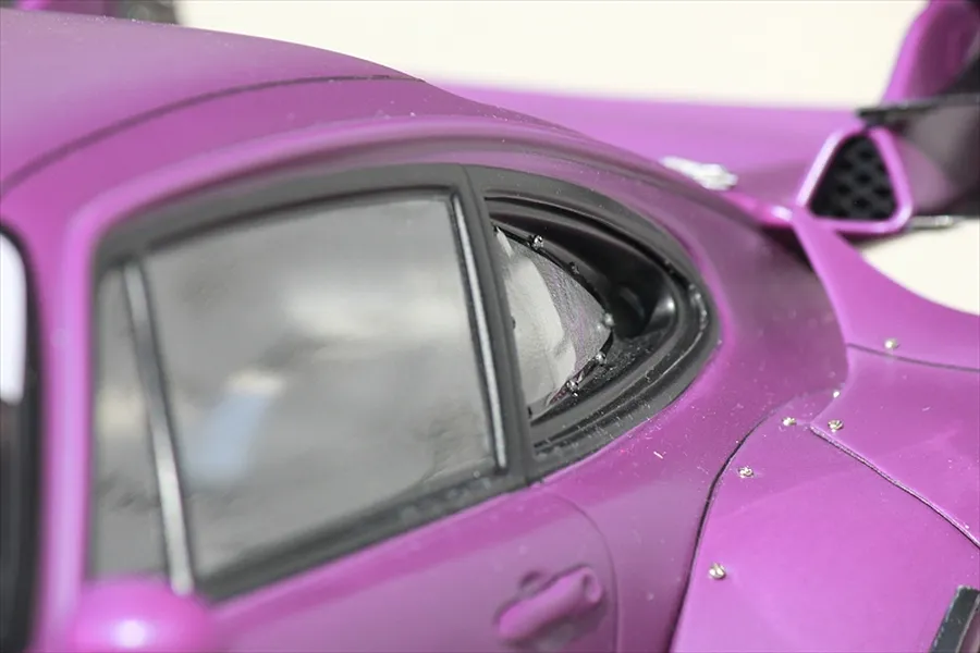 Close-up of a purple RC car body shell showing side windows, fender flare with mounting screws, and rear wing details.