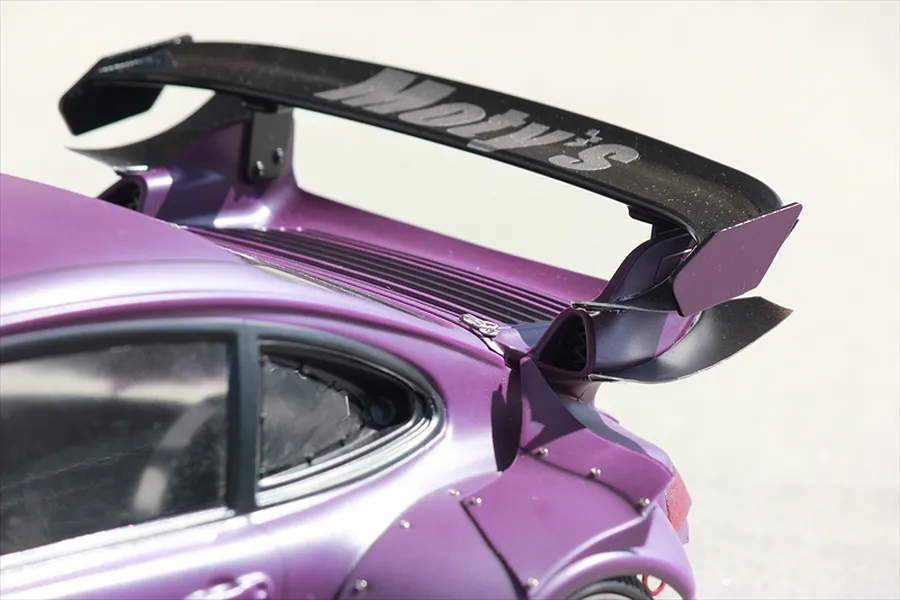 Close-up view of a purple RC car body shell featuring wide rear fenders, a large rear wing with Motys branding, and detailed window trim.