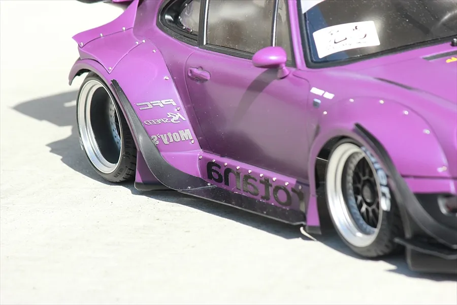 Close-up side view of a purple RC drift car body shell featuring wide fender flares and deep-dish wheels on a concrete surface.