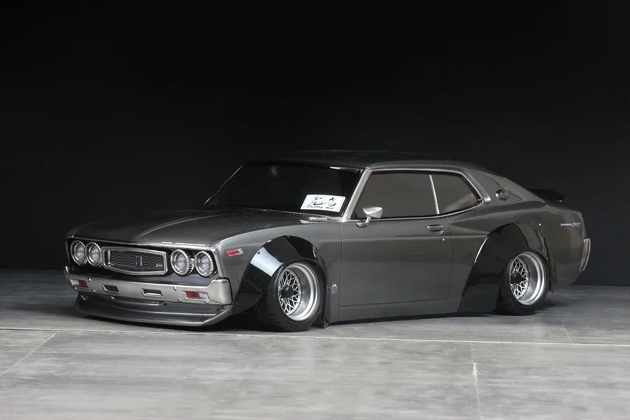Grey RC drift car body shell featuring prominent black overfenders and mesh wheels against a dark background.