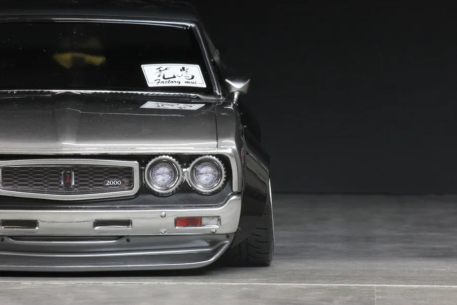 Close-up front view of an RC car body shell featuring overfenders, dual headlights, a front grille, and a bumper against a dark background.