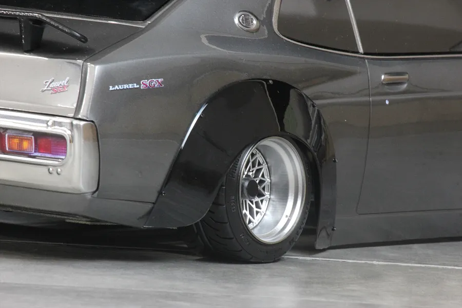 Close-up view of a dark grey RC car body shell fitted with a black overfender flare over the rear wheel and mesh rim.