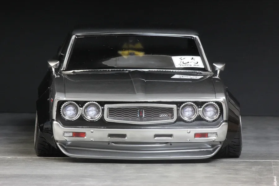 Front view of a custom grey RC drift car body showing overfenders and detailed grille against a dark background.