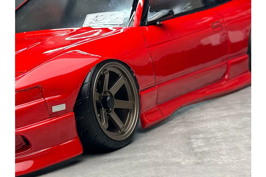 Close-up of a red RC drift car body showing the front wheel, side skirts, and painted body details.