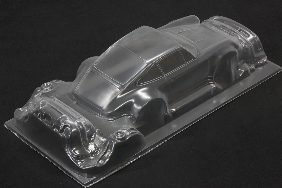 Unpainted clear polycarbonate RC car body shell of a widebody sports car on a dark surface.