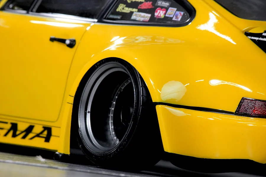 Close-up of the yellow RC car body showing the wide rear fender, deep dish wheel, and side decals.