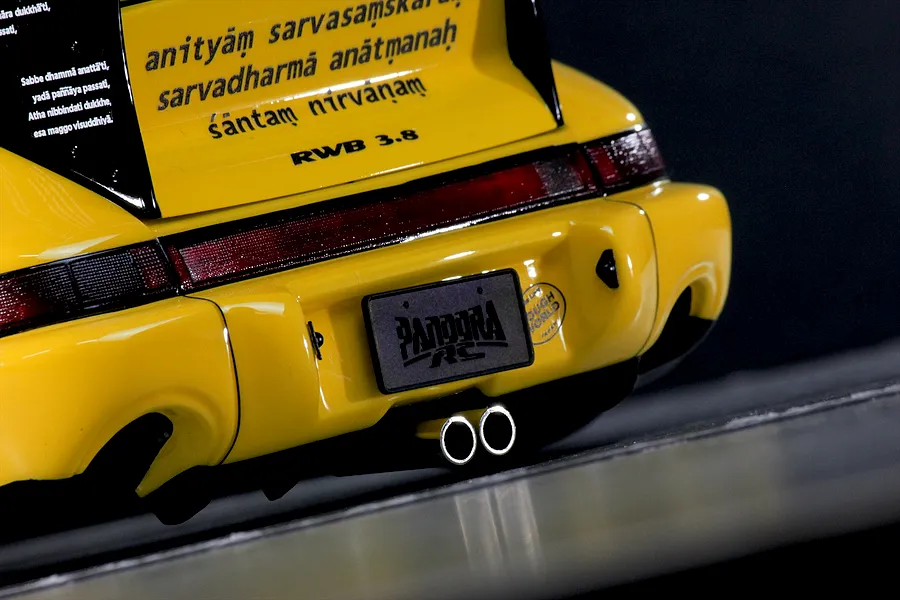 Close-up rear view of a yellow RC car body shell showing dual chrome exhaust tips, a large black spoiler with text, and a Pandora RC license plate.