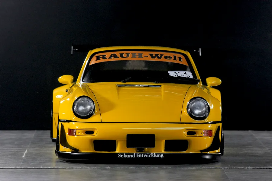 Front view of a yellow Pandora RC RWB 993 type body shell with wide fenders, front spoiler, and RAUCH-Welt windshield banner.