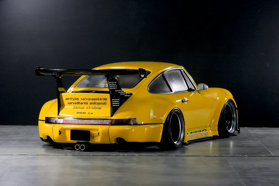 Rear three-quarter view of a yellow Pandora RC RWB 993 Type model car with wide fenders and a large wing on a dark background.