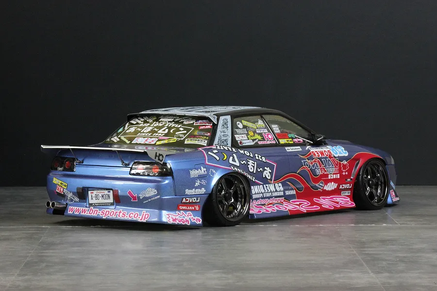 Rear-three-quarter view of a customized blue RC drift car body with extensive sponsor decals and a large rear wing.
