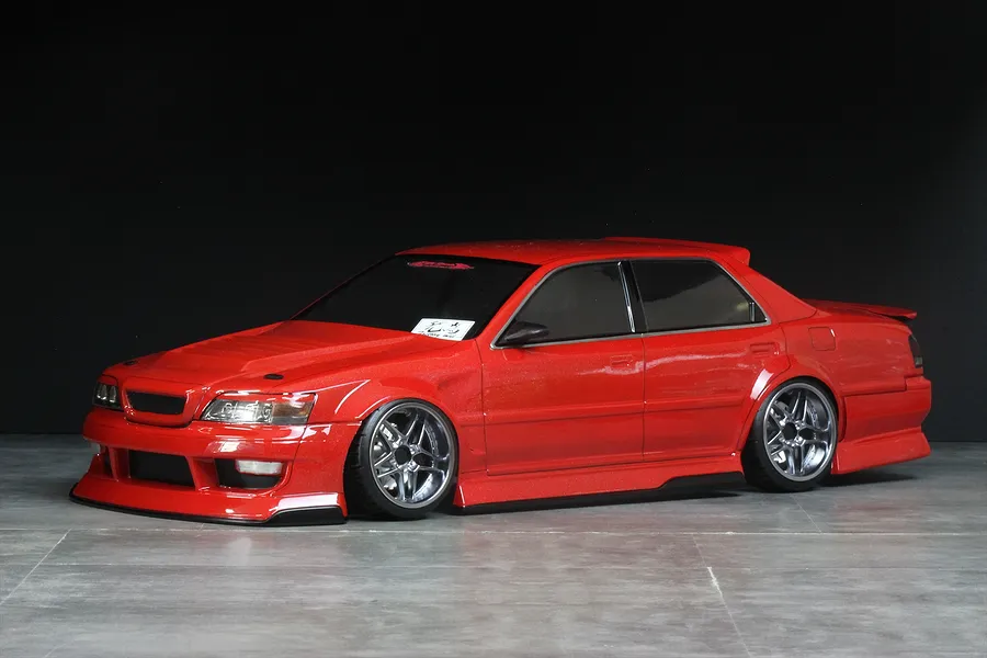 Red RC drift car body shell mounted on a chassis with chrome wheels against a black and grey studio background.