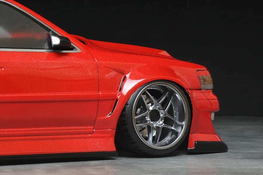 Close-up of the front quarter and wheel of a red RC drift car body with custom wide body styling and silver multi-spoke wheel.