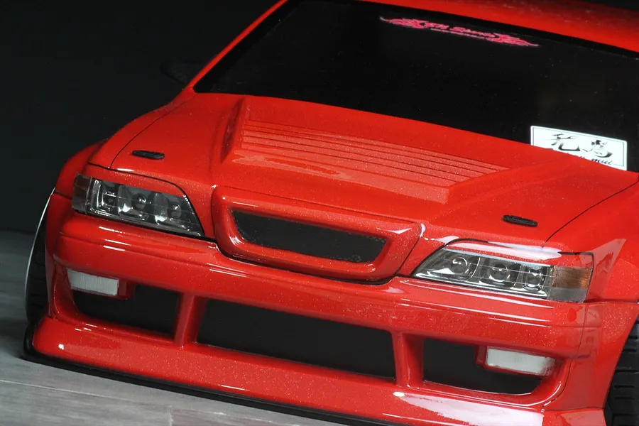 Close-up of the front end of a red RC drift car body showing detailed headlights, grille, and hood vents.
