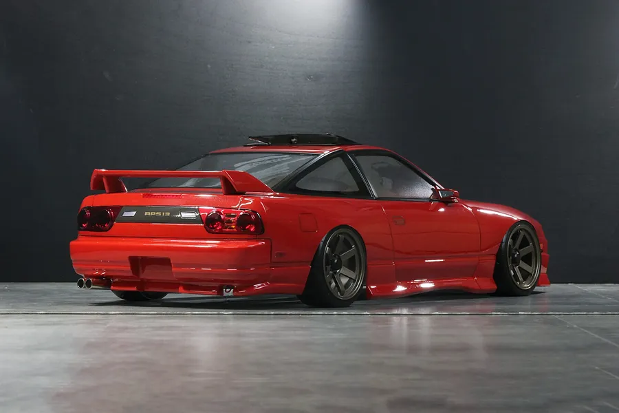 Rear three-quarter view of a red RC drift car body styled like a Nissan 180SX Kouki on a dark studio floor.