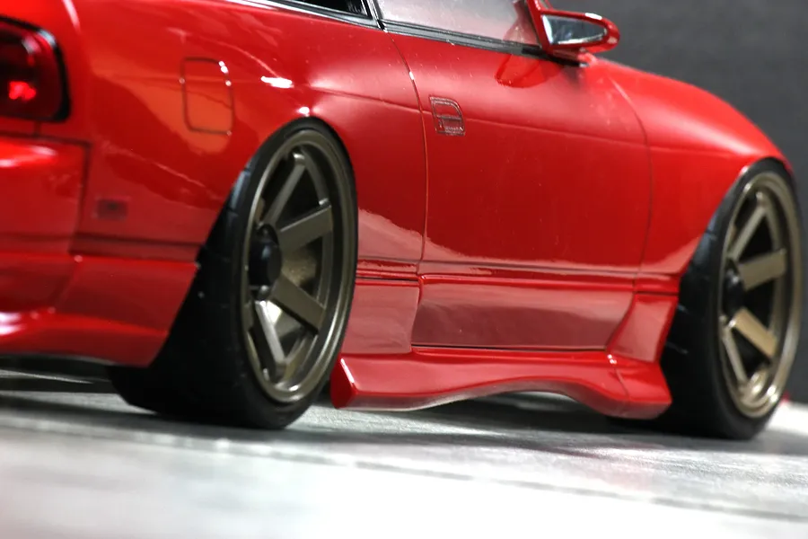 Close-up side profile view of a red RC drift car body showing custom wheels, side skirt, and low stance.