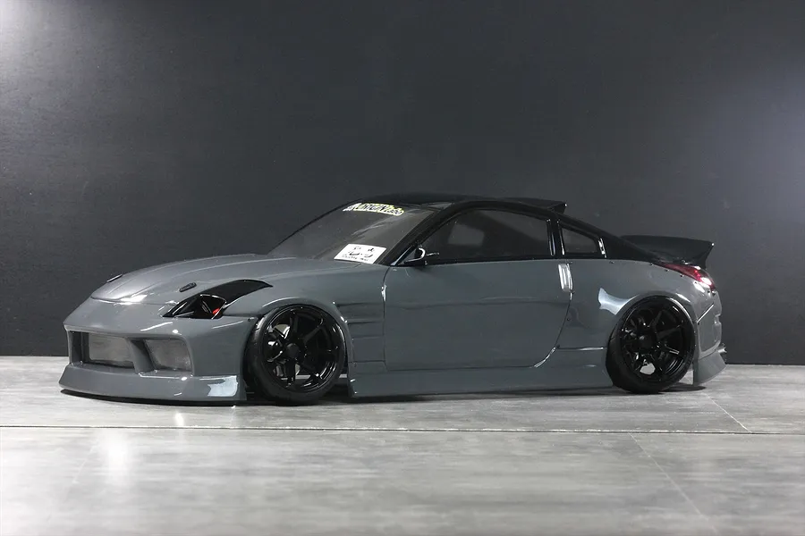 Grey Nissan 350Z RC drift car body shell with black wheels and aero kit displayed on a grey studio floor.