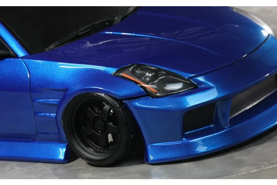 Close up view of the front quarter of a metallic blue RC drift car body shell showing front wheel, headlight and bumper detail.