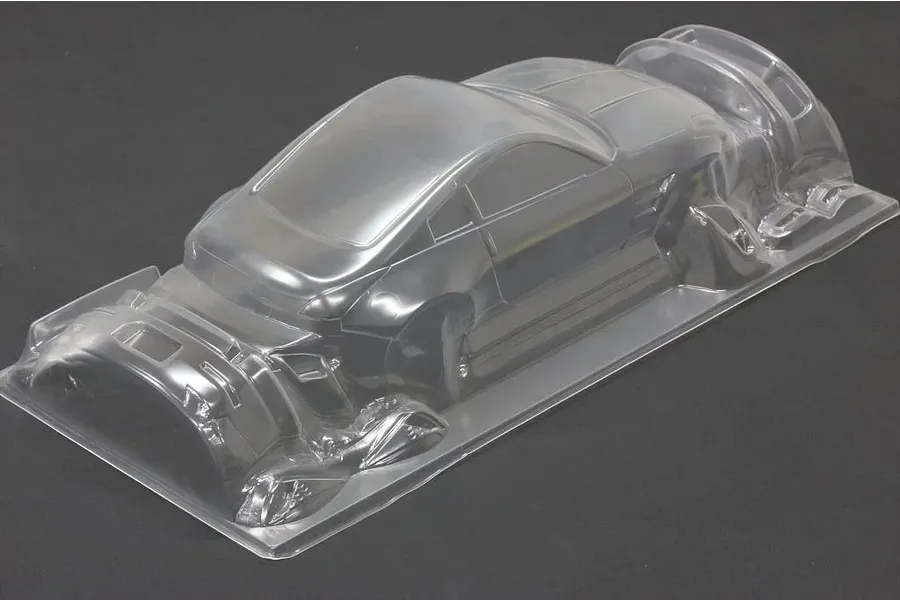 Unpainted clear polycarbonate RC car body shell on a dark surface, showing front and rear bumper parts molded into the sheet.