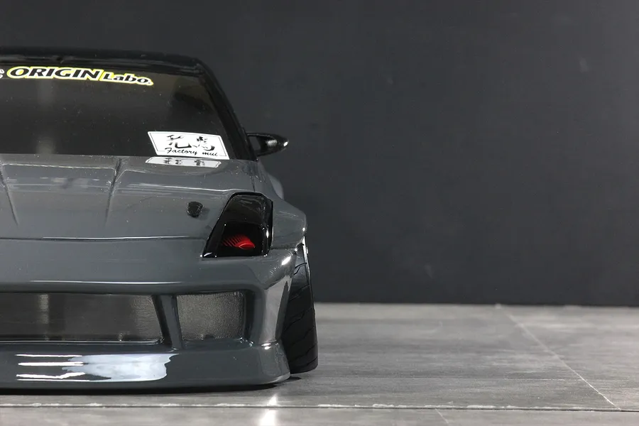 Front close-up view of a grey RC drift car body showing the front end, bumper, and tire against a dark background.