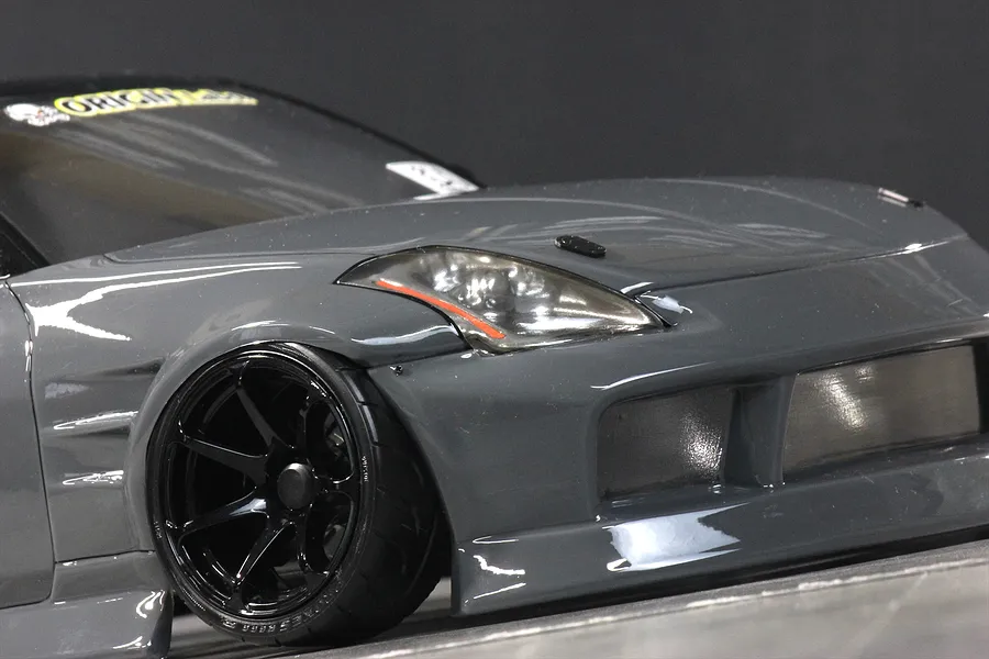 Close-up of the front left quarter of a grey RC drift car body showing the front wheel and headlight assembly.