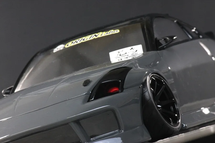 Low angle close-up of the front quarter of a glossy grey RC drift car body with black wheels and tinted windows.