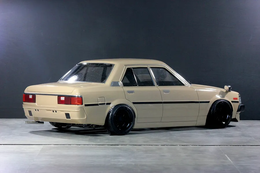 Rear-three-quarter studio shot of a tan Toyota Corolla KE70 RC drift car body on a dark grey surface.