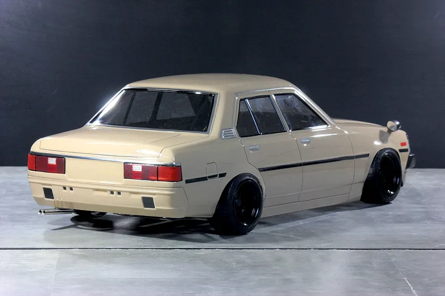Rear three-quarter studio view of a painted tan Toyota Corolla KE70 RC drift car body on a grey surface.