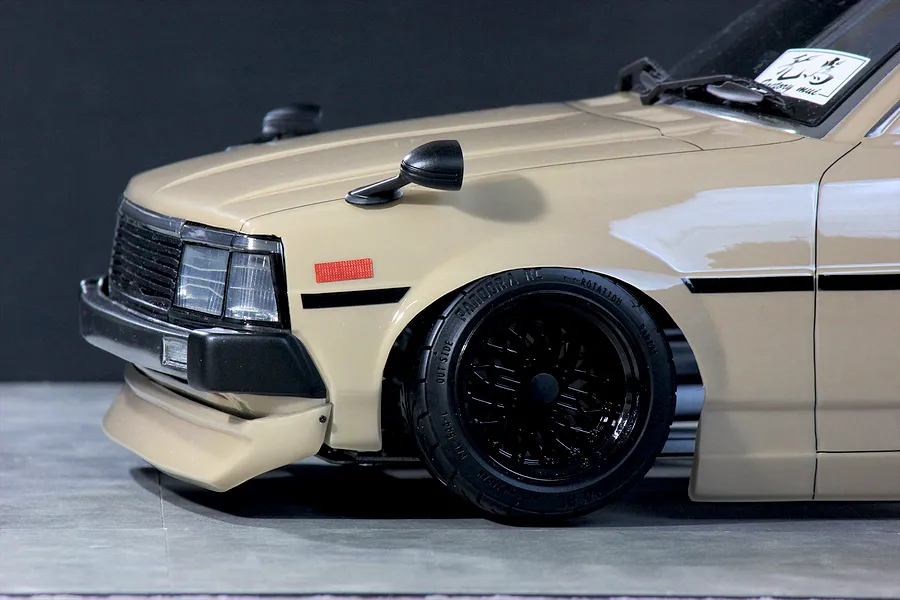 Close-up of the front quarter of a beige RC drift car body with black wheels and fender mirrors.