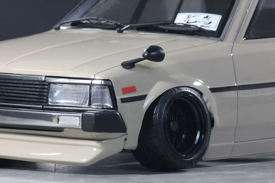 Close-up of a beige RC car body featuring front fender-mounted side mirror, black grille, and detailed wheel.