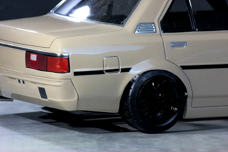 Close-up rear quarter view of a tan RC drift car body shell showing the tail light, rear wheel, and black mesh rim.