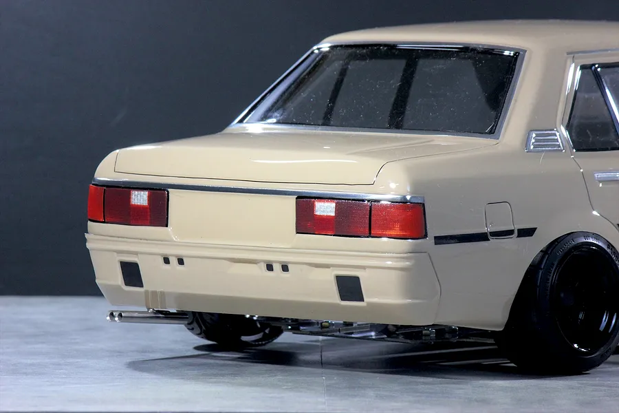 Rear-quarter view of the Pandora RC Toyota Corolla KE70 body shell in beige, showing taillights, dual exhaust, and black wheels.