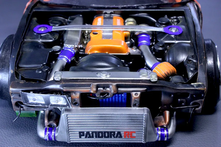 Top-down view of a detailed scale model RC car engine bay with an orange valve cover, front mount intercooler, and strut bar installed.