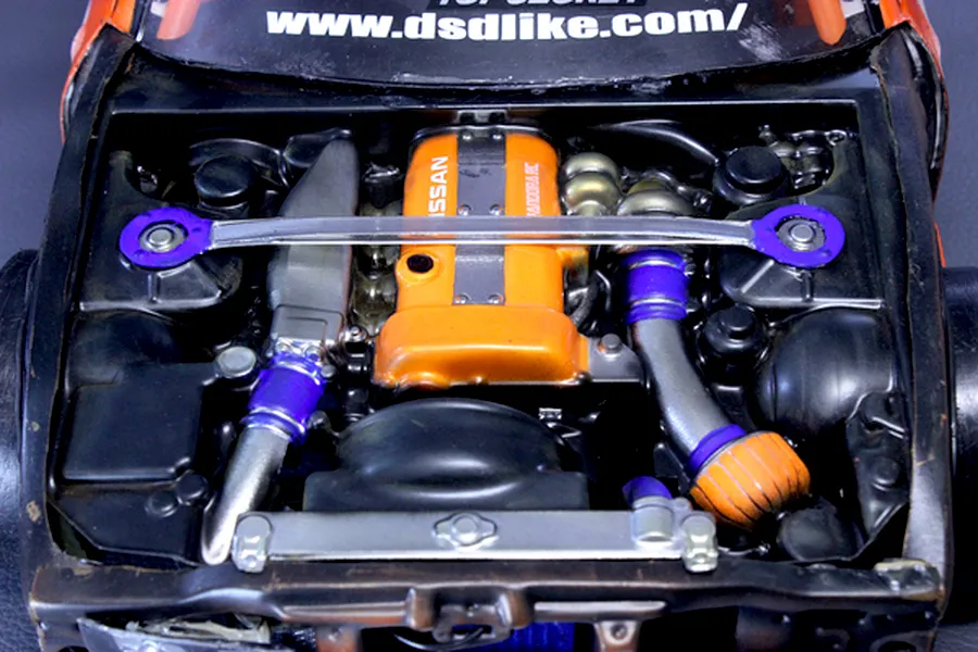 Close-up of a detailed scale model RC car engine bay with an orange Nissan engine and strut brace.