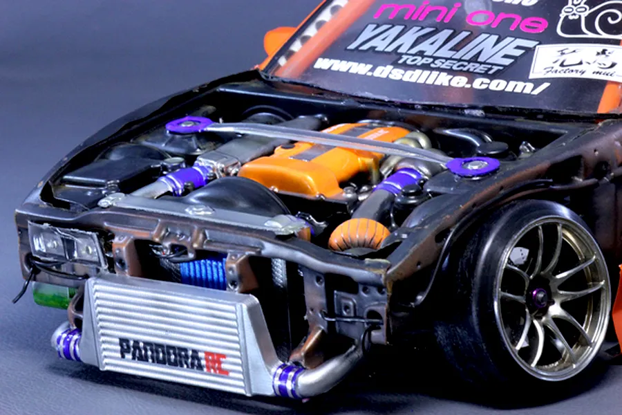 Close-up view of a detailed RC drift car engine bay with an orange valve cover, intercooler, and strut bar installed.