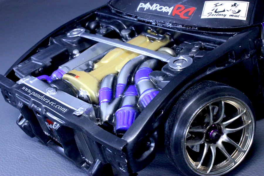 Detailed RC scale model engine bay with gold valve cover and purple hose accents installed in a black chassis.