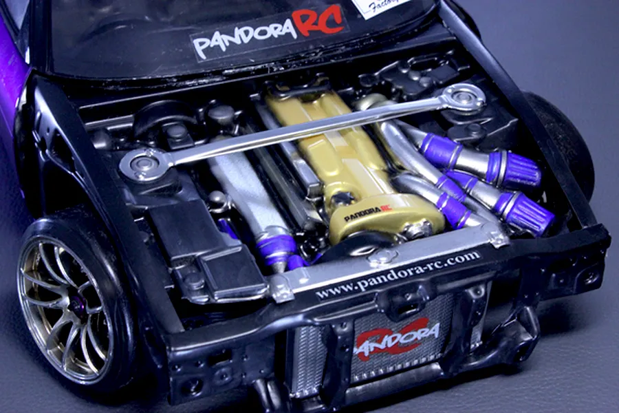 Close-up of a detailed Pandora RC scale model car engine bay installed in a vehicle, featuring a gold valve cover and strut bar.