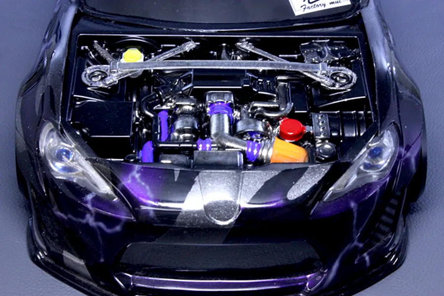 Detailed model car engine bay accessory installed in a black and purple RC car body with strut bar and aftermarket components.