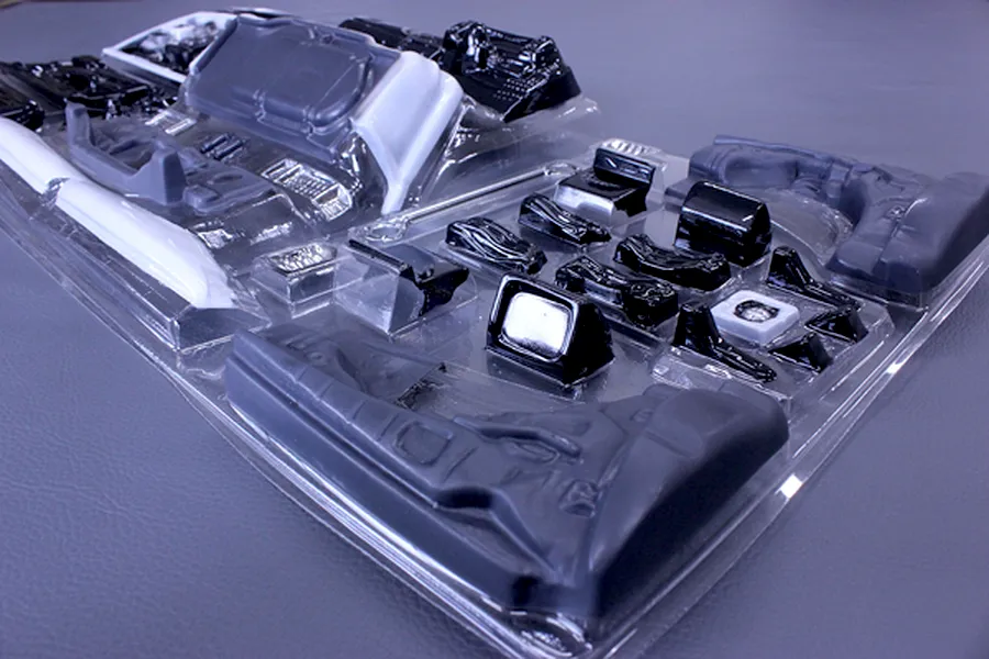 Unassembled plastic interior set parts in a clear blister pack for an RC car model on a grey surface.