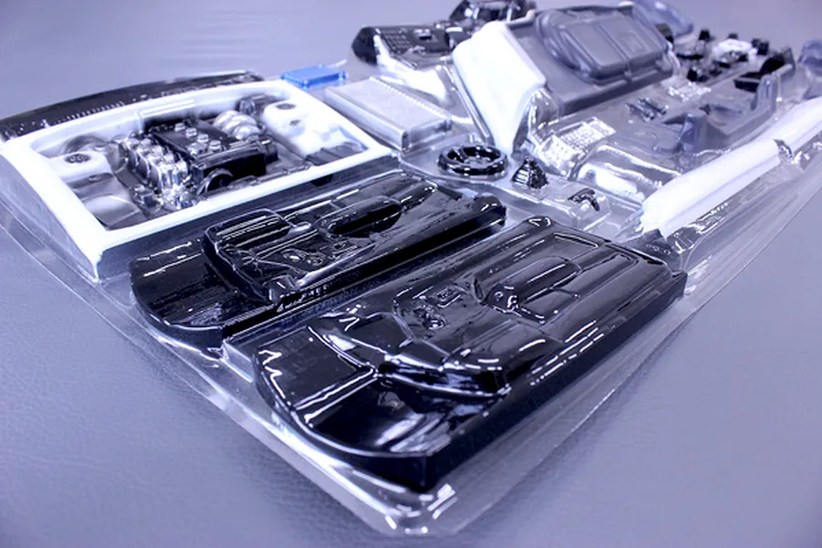 Unpainted RC car interior and engine accessory parts set in clear plastic blister packaging on a grey surface.