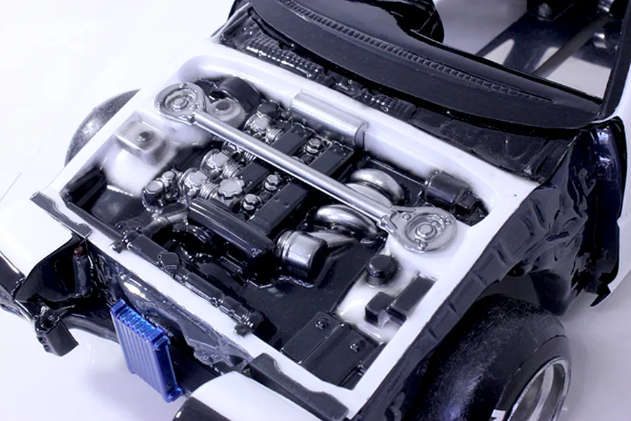 Close-up of a detailed model car engine bay showing a painted engine block, strut bar, and inner fender wells inside a white body shell.
