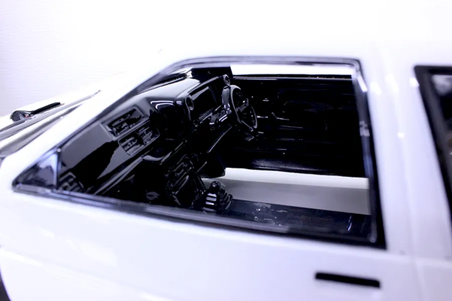 Close-up of a detailed black RC car interior with dashboard and steering wheel inside a white body shell.