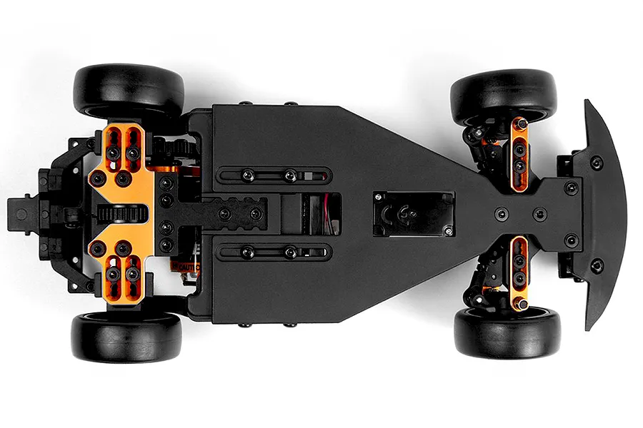 Top-down studio view of an RC car chassis showcasing its black deck, black rubber wheels, and bright orange aluminum suspension mounts against a plain white background.