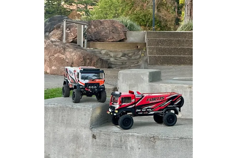 Two HobbyPlus DKR-4 Fortis RC trucks in red and white liveries parked on concrete steps outdoors.