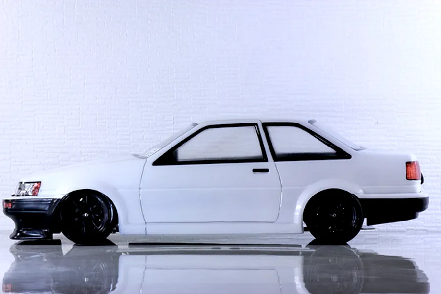 Side profile view of a white Toyota AE86 Corolla Levin RC car body with black wheels and bumpers.