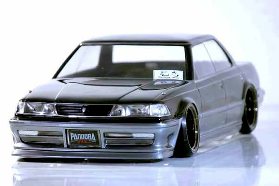 Studio shot of a painted Pandora RC Toyota Mark2 JZX81 RC drift car body shell in black and silver on a reflective white surface.